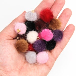 May include: A collection of colourful faux fur pom poms with gold metal loops. The pom poms are in various colours, including pink, red, brown, black, white, and purple.