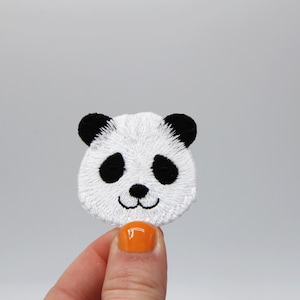 Könnte beinhalten: Weißer gestickter Panda-Gesichts-Patch mit schwarzen Augen und Nase.