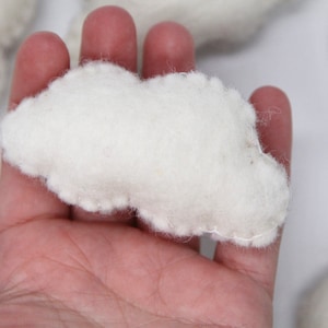 Puede incluir: Una nube de fieltro blanco con un borde cosido. La nube está siendo sostenida en una mano.