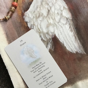 May include: A white card with the number 19 and the word "Grace" printed on it. The card has a blue and white image of an angel wing and text that reads "Here May Be Your Eleventh Hour And a Blessing from An Unknown Source Here Is When Grace Sent Your Second Wind to Guide You Back on Course."