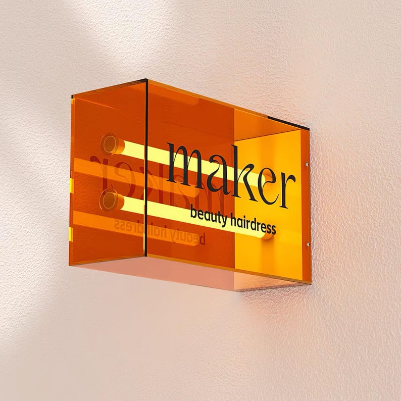 May include: Orange acrylic sign with the text "maker beauty hairdresser" in black lettering. The sign has a glowing yellow light inside.