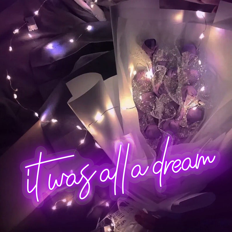 May include: A bouquet of purple flowers wrapped in white tissue paper with a string of white fairy lights wrapped around it. The text "it was all a dream" is written in neon purple letters.