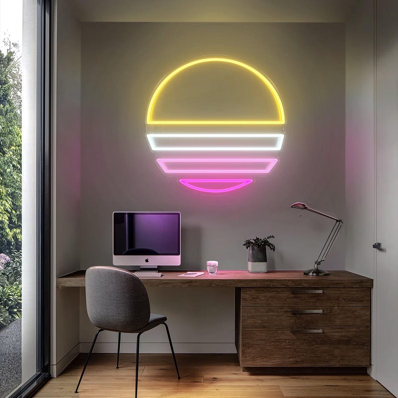 May include: A neon sign in the shape of a sunset with yellow, white, and pink colors. The sign is mounted on a wall above a desk with a computer, a lamp, and a chair.