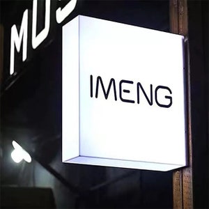May include: A white rectangular sign with black lettering that reads "IMENG". The sign is mounted to a wooden surface.