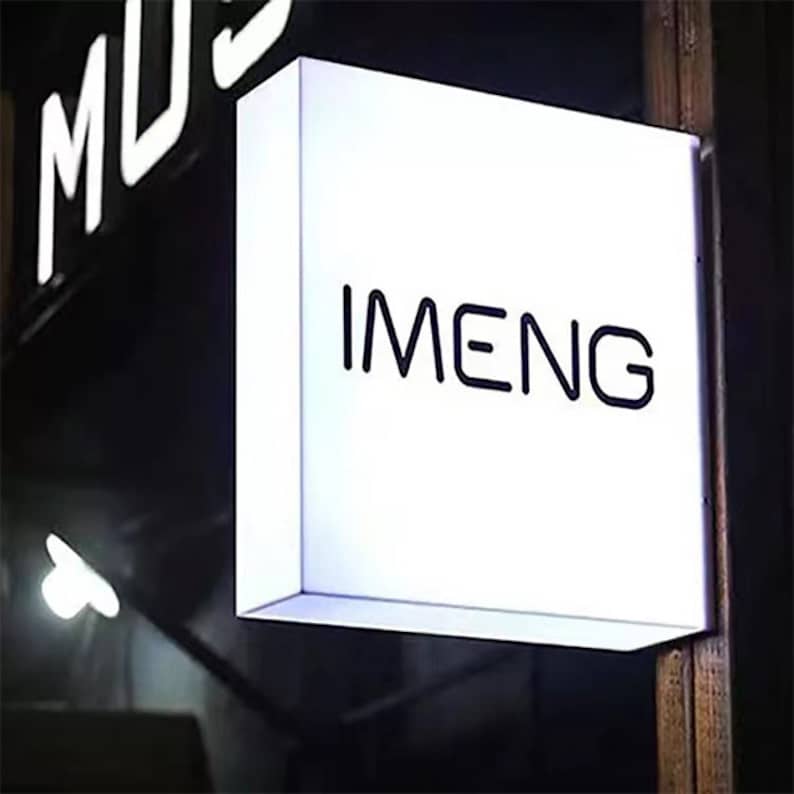 May include: A white rectangular sign with black lettering that reads "IMENG". The sign is mounted to a wooden surface.