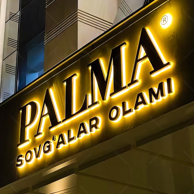 May include: Illuminated sign for "PALMA SOVG'ALAR OLAMI" in a nighttime setting. The sign features bold, black lettering with a bright yellow glow, creating a striking contrast against the dark background. The design includes a registered trademark symbol.