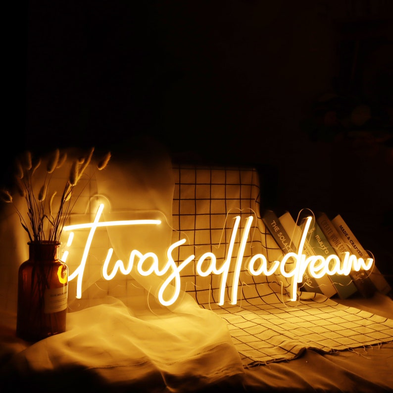 May include: A neon sign with the text "It was all a dream" in white neon letters on a black background. The sign is sitting on a white and brown checkered surface.