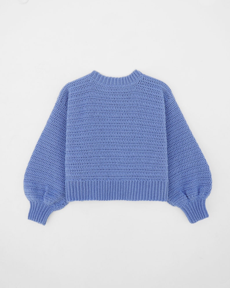 May include: A light blue crocheted sweater with long sleeves and a round neckline.