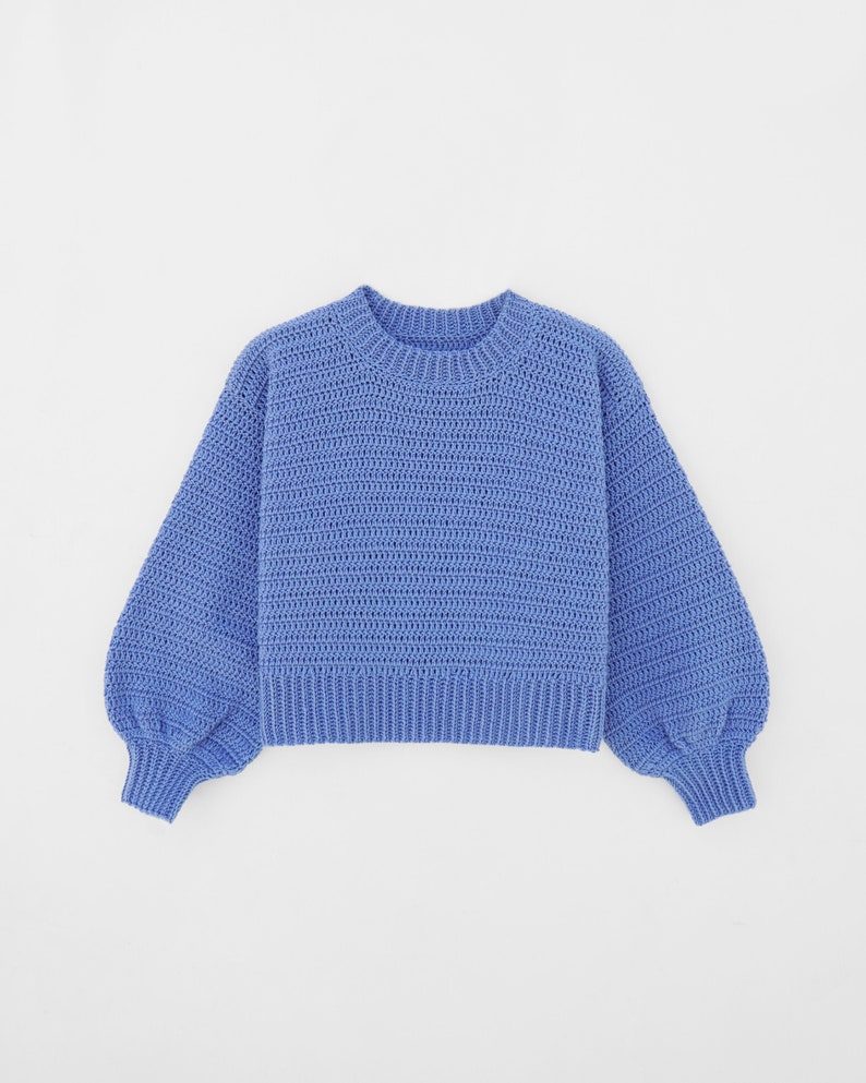 May include: A light blue knitted sweater with long sleeves and a round neckline.