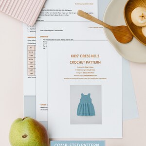 May include: A crochet pattern for a kids' dress, titled "Kids' Dress No. 2 Crochet Pattern". The pattern is designed by Daisy & Peace and includes 8 pages. A photo of a completed blue dress is shown.