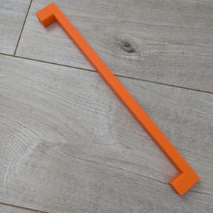 Peut inclure: Poignée de placard orange de forme carrée. La poignée est en plastique et a une surface lisse.
