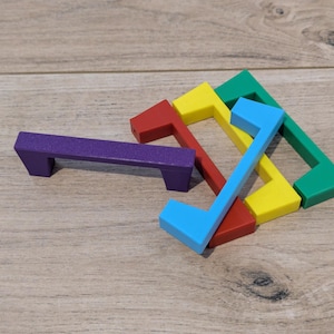 May include: A selection of brightly coloured wooden shapes, including a purple rectangular handle and angular pieces in red, yellow, blue, and green. The shapes are arranged on a light brown wooden surface.