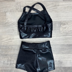 Peut inclure: Ensemble de danse noir brillant compos&eacute; d'un haut et d'un short. Le haut a un design de bretelles crois&eacute;es et le short a une taille haute.