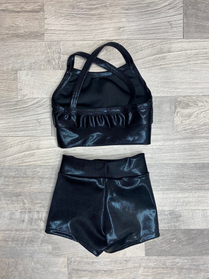 Peut inclure: Ensemble de danse noir brillant compos&eacute; d'un haut et d'un short. Le haut a un design de bretelles crois&eacute;es et le short a une taille haute.