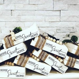 May include: A stack of wooden blocks with the words "Home Sweet Home" painted on them. The blocks are decorated with burlap and wooden beads.
