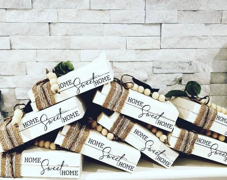 May include: A stack of wooden blocks with the words "Home Sweet Home" painted on them. The blocks are decorated with burlap and wooden beads.