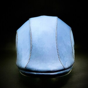 May include: A light blue flat cap with a stitched design. The cap is made of a soft, textured material.