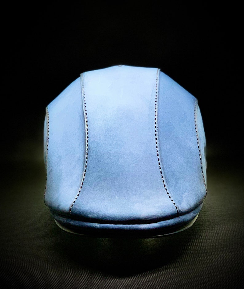 May include: A light blue flat cap with a stitched design. The cap is made of a soft, textured material.