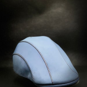 May include: A light blue flat cap with a stitched design.