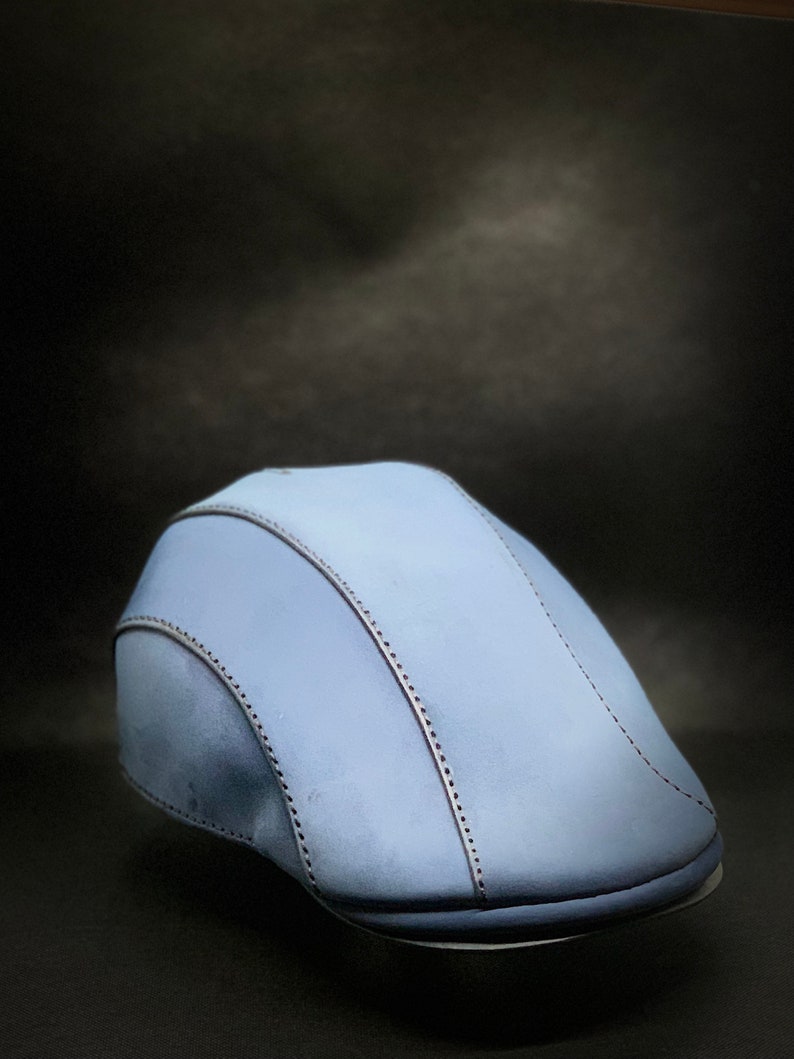 May include: A light blue flat cap with a stitched design.