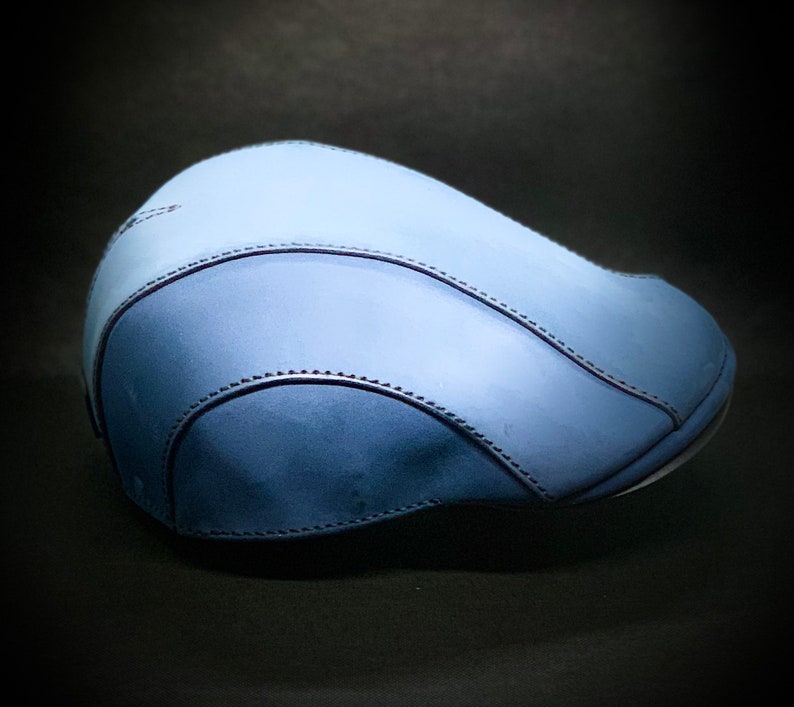 May include: A blue leather newsboy cap with a stitched seam detail.