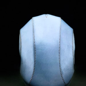 May include: A light blue helmet with a stitched seam down the centre and on each side. The helmet is made of a soft, pliable material.