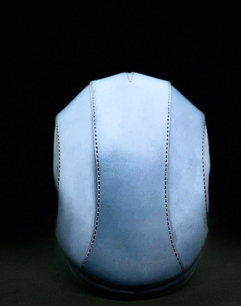 May include: A light blue helmet with a stitched seam down the centre and on each side. The helmet is made of a soft, pliable material.