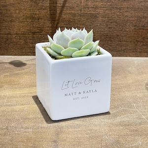 May include: White square succulent planter with the text "Let Love Grow" and the names "Matt & Kayla" and the date "EST. 2023".