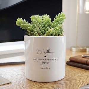 May include: A white cylindrical ceramic planter containing a green succulent plant. The front of the planter features black printed text that reads: Ms. William, a small heart symbol, THANK YOU FOR HELPING ME grow, and Love, Amy.