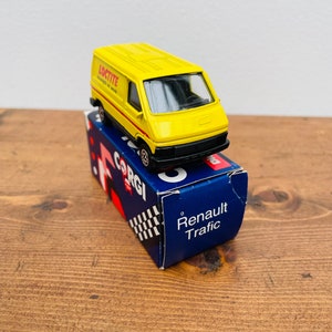 Puede incluir: Una furgoneta de juguete amarilla con la marca "Loctite" en el lateral, sentada sobre una caja azul y roja que dice "Renault Trafic".