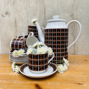 May include: A vintage brown and black geometric patterned tea set with a teapot, creamer, sugar bowl, cups, and saucers. The set is arranged on a wooden table with white flowers.