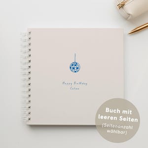Puede incluir: Un cuaderno de espiral beige claro con una ilustración de bola de discoteca azul y el texto manuscrito "Happy Birthday Celine". Un estuche blanco y un bolígrafo dorado son visibles. El cuaderno tiene páginas en blanco.