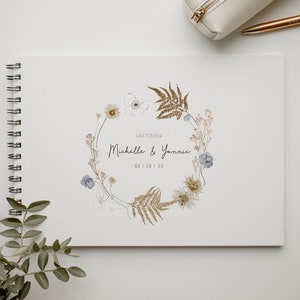 Könnte beinhalten: Ein weißes, spiralgebundenes Gästebuch mit einem floralen Kranzdesign in Braun-, Blau- und Weißtönen. Der Text "Gastebuch Michelle & Yannic 09 | 09 | 23" ist auf dem Einband gedruckt.