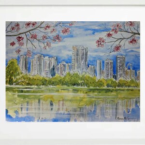 May include: Watercolour painting of a city skyline reflected in a lake. The city is in the background and the lake is in the foreground. There are trees in the foreground and pink flowers in the top left and right corners of the painting.