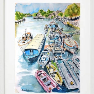 May include: Watercolour painting of a harbour scene with numerous boats moored along a pier. The boats are of various sizes and colours, including white, blue, and pink. The artwork is framed in a white border, with a river and buildings in the background.