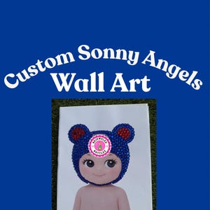 Może przedstawiać: Niestandardowa grafika ścienna Sonny Angels. Wydruk na pł&oacute;tnie przedstawiający postać z kresk&oacute;wki z niebieską, wysadzaną klejnotami czapką niedźwiedzia oraz r&oacute;żową i białą naklejką. Tło jest żywo niebieskie.