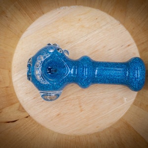 May include: A blue glass smoking pipe with a glitter finish. The pipe has a round bowl and a straight stem.
