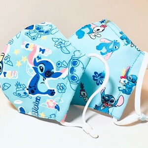 May include: Two blue face masks with white elastic ear loops. The masks feature a repeating pattern of Stitch from Lilo & Stitch, with the text "Aloha" and other small designs.