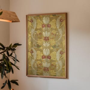 Könnte beinhalten: Ein gerahmtes Kunstwerk mit einem detaillierten Blumenmuster in Gold-, Rot- und Cremetönen. Das Kunstwerk wird an einer neutralfarbenen Wand ausgestellt und verleiht dem Raum Eleganz. Der Rahmen ist aus Holz.