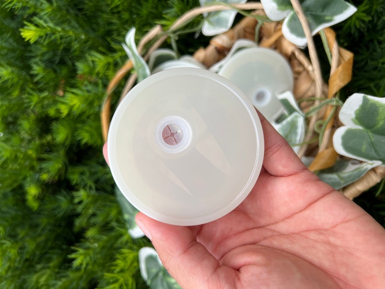 May include: A white plastic lid with a small hole in the center. The lid is smooth and has a slightly raised edge.