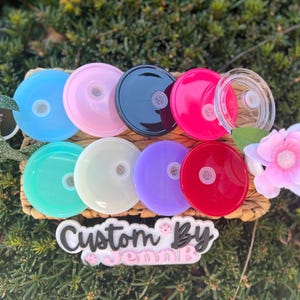 May include: Assortment of 10 colorful and clear plastic lids with a small hole in the center. The lids are arranged in a circle on a woven surface. The text "Custom By Jenn B" is visible below the lids.