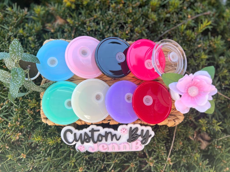 May include: Assortment of 10 colorful and clear plastic lids with a small hole in the center. The lids are arranged in a circle on a woven surface. The text "Custom By Jenn B" is visible below the lids.