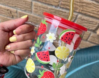 Könnte beinhalten: Eine durchsichtige Glas-Tasse mit rotem Deckel und gelbem Strohhalm. Die Tasse hat ein buntes Design mit Erdbeeren, Zitronen und Wassermelonen-Scheiben.