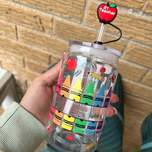 May include: Clear plastic reusable water bottle with a rainbow of crayons, pencils, and other school supplies printed on the side. The bottle has a red apple lid with the text "#1 Teacher" on it.