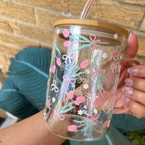 May include: A clear glass mug with a bamboo lid and a pink and green floral design. The mug has a straw and a handle.