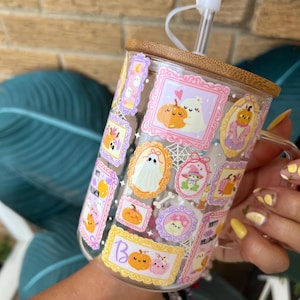 May include: A clear glass mug with a bamboo lid and straw, decorated with Halloween-themed illustrations in ornate frames. The mug features pumpkins, ghosts, and the word "Boo". The straw has a white flower-shaped stopper.