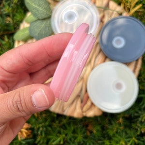 May include: A close-up of a pink, clear plastic lid with a white ring around the edge. The lid is being held by a hand.