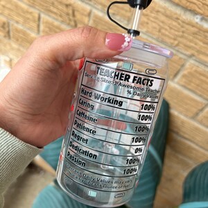 May include: A clear plastic tumbler with a black lid and straw. The tumbler has a label that reads "Teacher Facts" and lists various qualities with percentages, such as "Hard Working 100%", "Caring 100%", "Caffeine 100%", "Patience 100%", "Regret 0%", "Dedication 100%", and "Passion 100%".