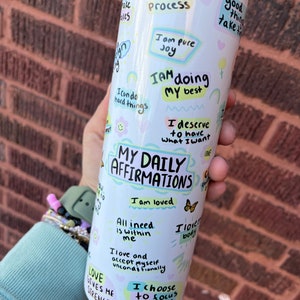 May include: White stainless steel tumbler with a colorful design and positive affirmations. The tumbler features phrases like "Trust the Process", "I am pure Joy", "I am doing my best", "I deserve to have what I want", "My Daily Affirmations", "I am loved", "All I need is within me", "I love and accept myself unconditionally", "I choose to focus on the good", and "Love gives me strength".