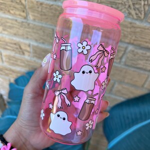 May include: A pink-tinted glass tumbler with a matching lid, decorated with cartoon ghosts, bows, flowers, and drink illustrations. The tumbler is designed for cold beverages.